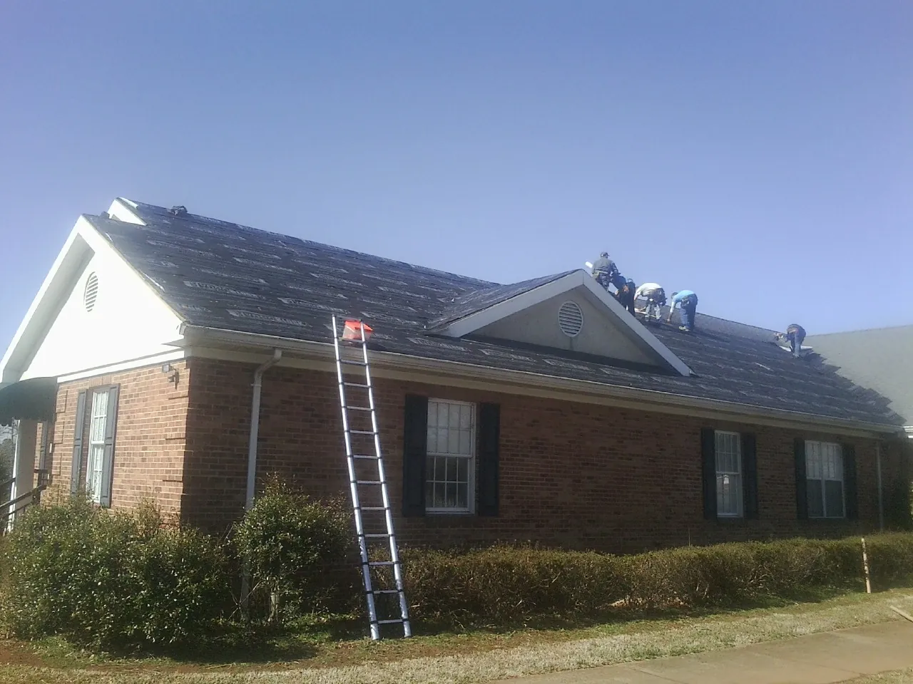 Crew tearing shingles off a brick ranch roof with a ladder set — Metal Roof Repair work by our crew in Red Bud