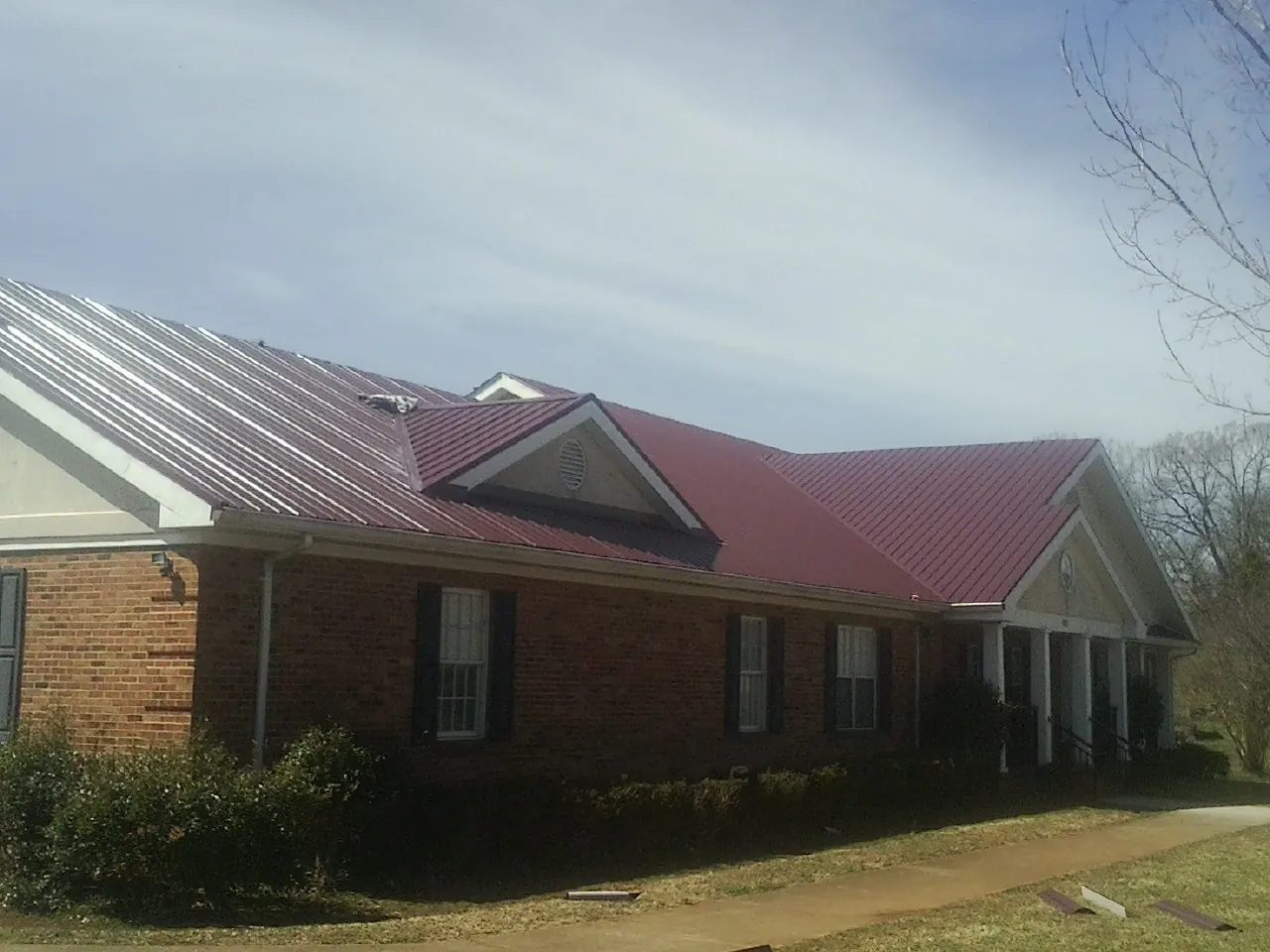 Red metal roof with gabled entries on a long brick building, from a Hail Damage Roof Repair job in Red Bud