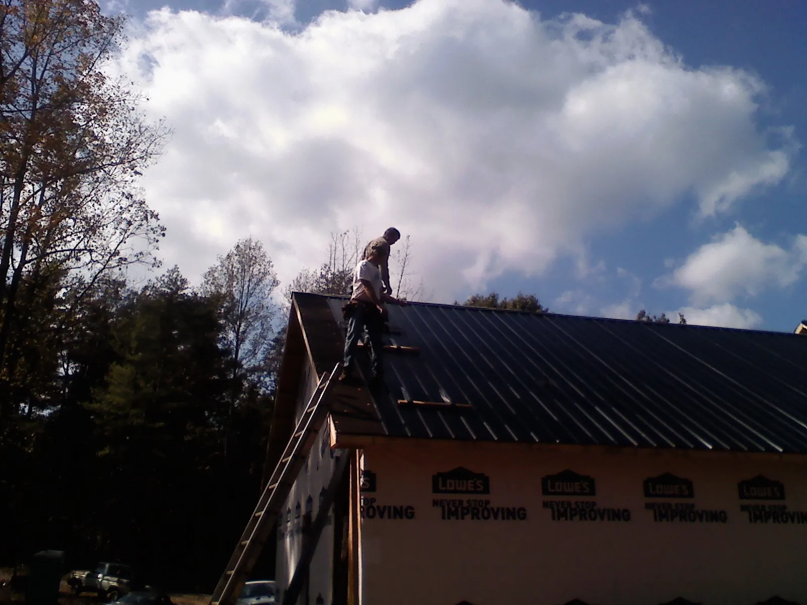 Roofer fastening dark metal panels high against a cloudy sky, from a Roof Inspection job in Red Bud